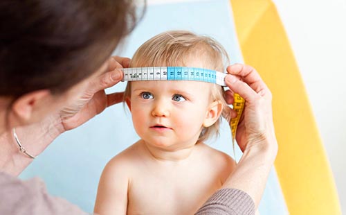 Врач измеряет окружность черепа ребёнка, чтобы узнать правильно ли он развивается