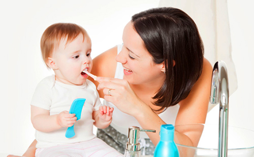 Черноволосая мама смеётся и чистит зубки своему малышу