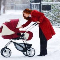 Мама в красном пальто гуляет с ребёнком в коляске зимой