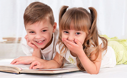 Мальчик и девочка читают книгу и смеются