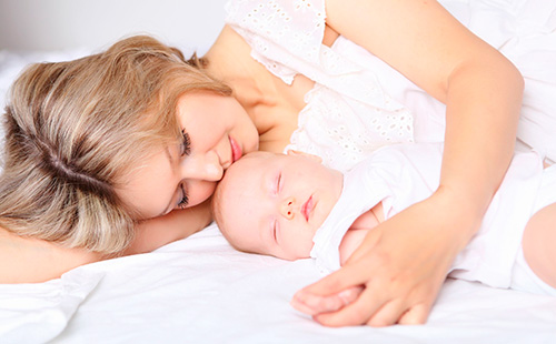 Молодая мама лежит возле ребенка