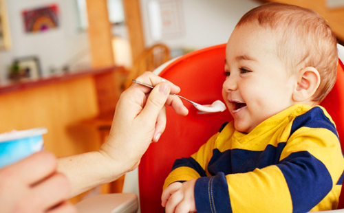 Радостный малыш ест с ложечки биокефир