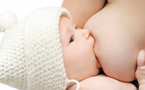 Малыш в вязаной белой шапочке сосет грудь
