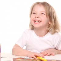 Маленькая девочка рисует карандашами и улыбается