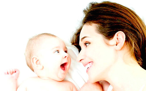 Молодая мама смотрит на малыша и смеется