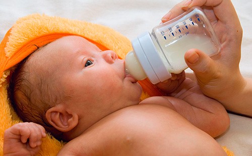 Новорожденный пьет молоко из бутылочки