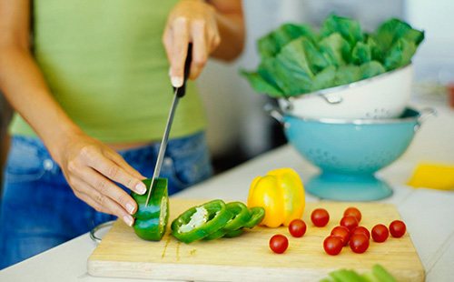 Женщина режет сладкий перец зеленого цвета