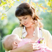 Юная мама среди весенней листвы держит на руках своё первое дитя