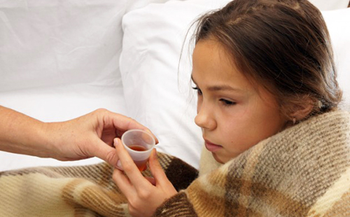 Больная девочка под шерстяным одеялом собирается выпить лекарство