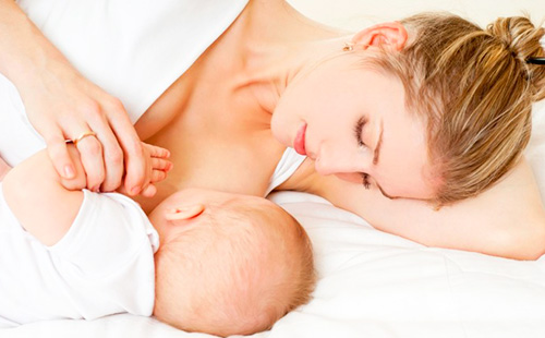 Молодая женщина лежа кормит грудью малыша