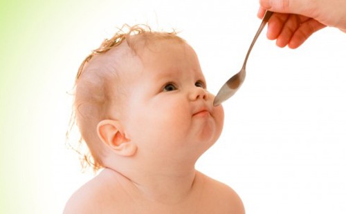 Младенец с пухлыми щёчками недоверчиво смотрит на ложку с лекарством