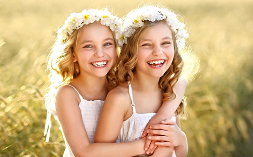 Смеющиеся девочки-близняшки в венках из полевых ромашек