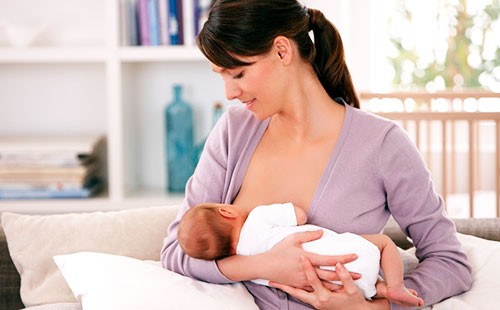 Молодая женщина кормит ребенка грудью