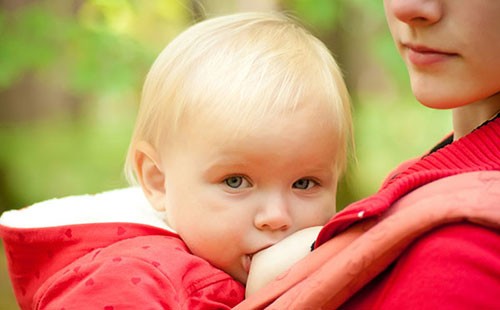 Ребенок в красной куртке сосет грудь