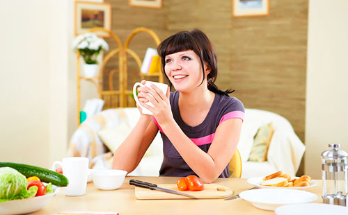 Молодая женщина сидит за столом и пьет чай