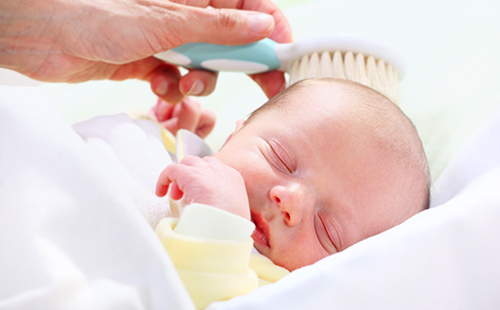 Почти лысого новорожденного осторожно причёсывают щёткой