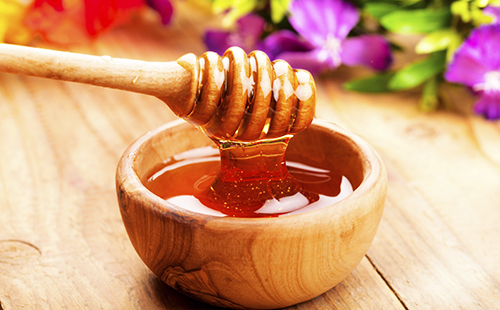 Мёд в деревянной плошке на фоне ярких цветов