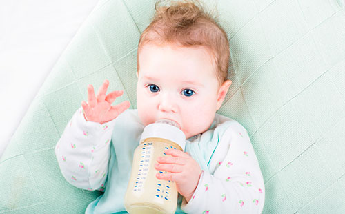 Маленький ребенок пьет молочную смесь из бутылки