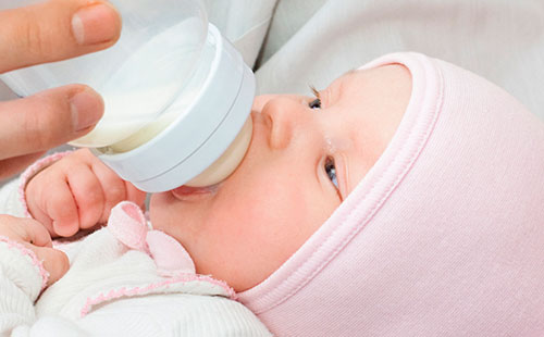 Младенец сосет молоко из бутылочки