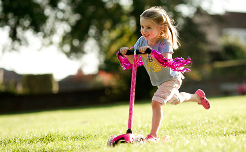 Девчушка катается в парке на розовом самокате