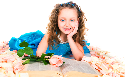 Маленькая принцесса в голубом платье устроилась с большой книгой среди роз