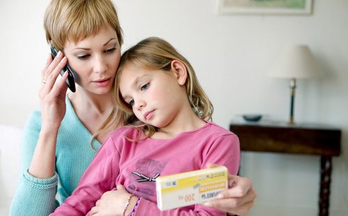 Мама держит на руках девочку и читает аннотацию к таблеткам
