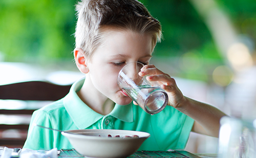 Мальчик за завтраком пьёт воду из стакана